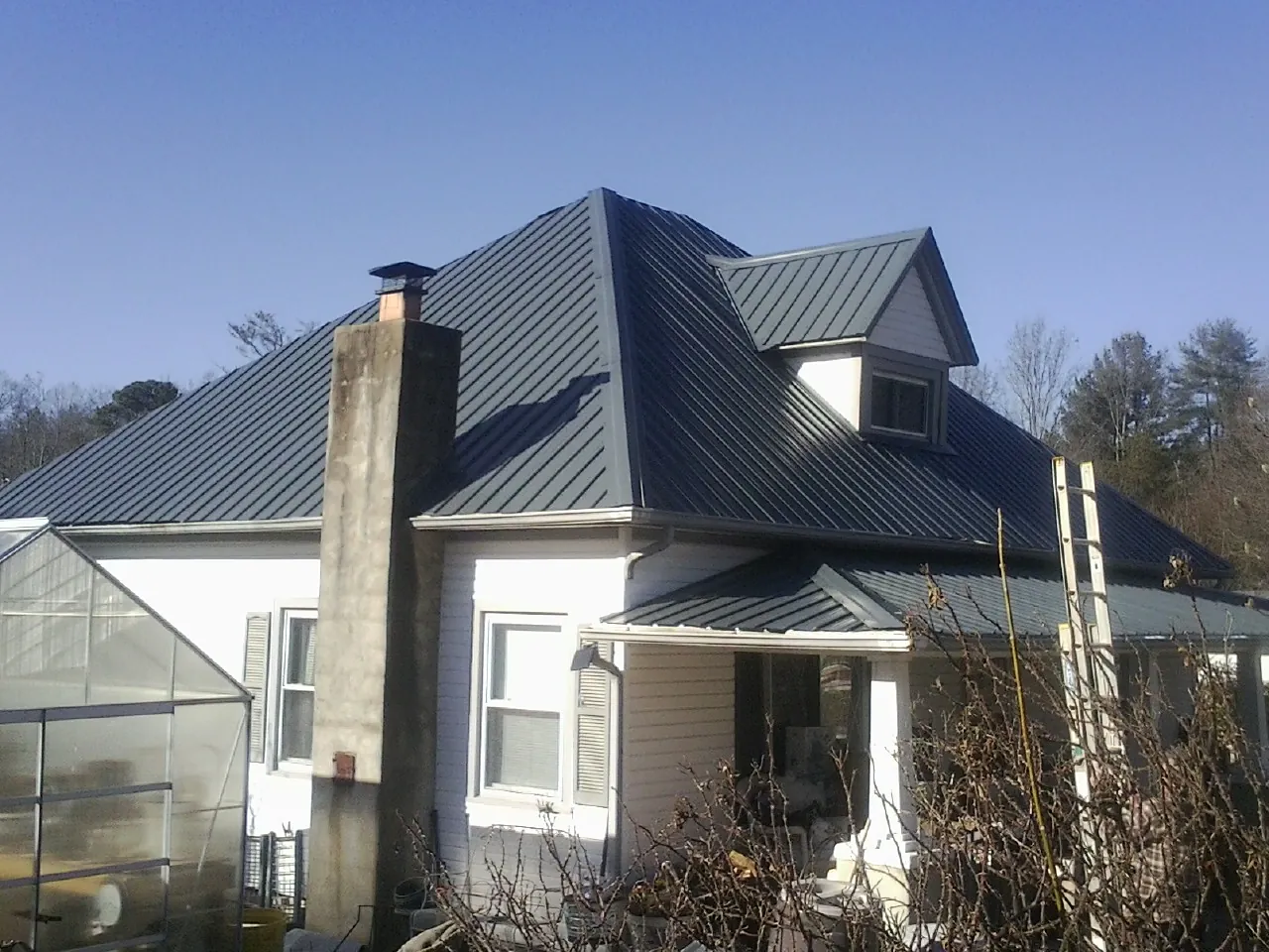 Dark blue standing seam metal roof on a white farmhouse with dormer in Alden