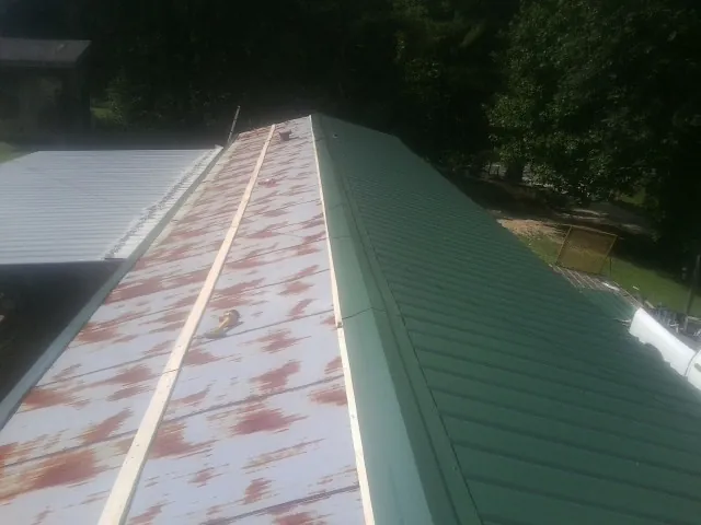 Old rusted panels beside newly installed green metal roofing — Wind Damage Roof Repair by Roofing Brothers in Alden