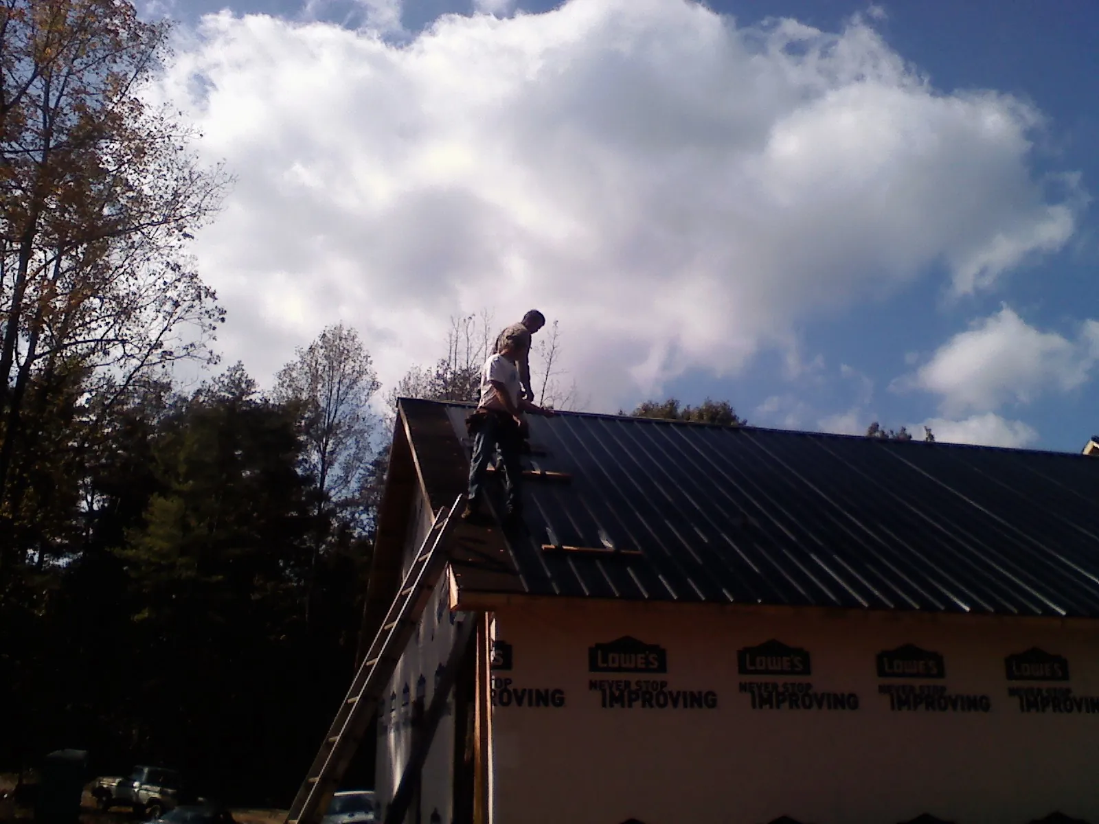 Roofer fastening dark metal panels high against a cloudy sky, from a Roof Inspection job in Alden