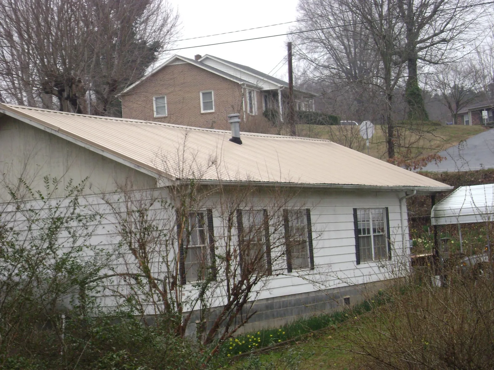 Tan metal roof on a white sided house set into a hillside — Commercial Roofing by Roofing Brothers in Alden